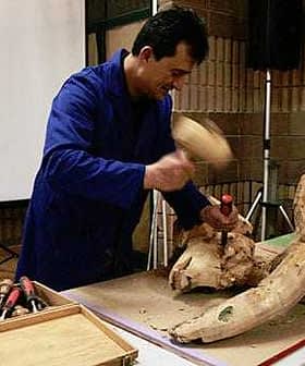 A woodworker using a chisel and hammer to carve a wooden sculpture during a demonstration. - Olive Oil Times