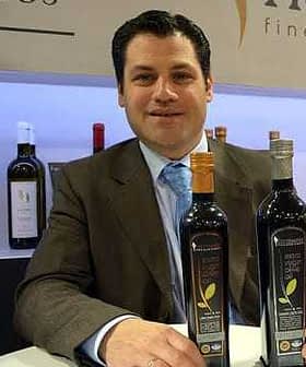 A man in a suit sitting at a table with two bottles of olive oil in front of him. - Olive Oil Times