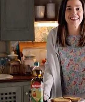 Woman smiling while holding a plate of toast next to a bottle of Carbonell olive oil in a kitchen. - Olive Oil Times