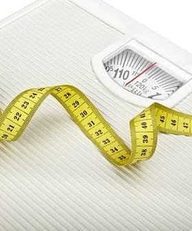White analog bathroom scale with a measuring tape curled around it. - Olive Oil Times