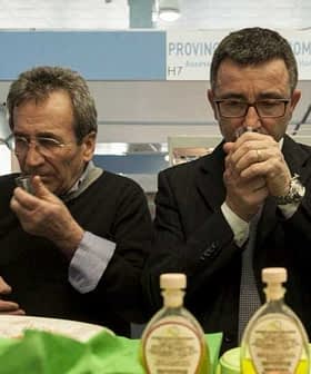 Two men tasting olive oil from small cups at an event, focusing on the aroma and flavor. - Olive Oil Times