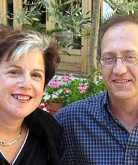 Two individuals smiling while posing for a photograph outdoors, with plants in the background. - Olive Oil Times