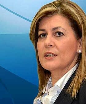 Woman with light brown hair wearing a dark blazer and white shirt against a blue background. - Olive Oil Times