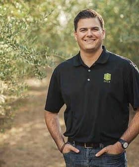 Man wearing a black polo shirt and jeans standing in an olive grove with trees in the background. - Olive Oil Times
