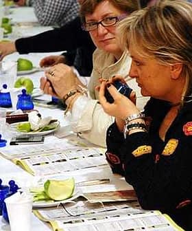 Two women participating in an olive oil tasting event, examining samples at a table. - Olive Oil Times