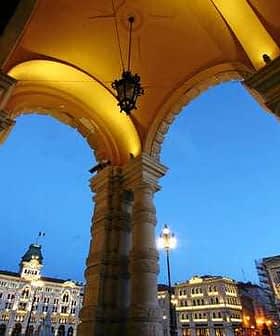 Archway with decorative columns and lanterns, overlooking a city square in Trieste during twilight. - Olive Oil Times