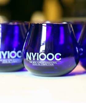 Set of blue glasses featuring the logo of the New York International Olive Oil Competition. - Olive Oil Times