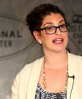 Woman with glasses speaking during a presentation at a cultural center event. - Olive Oil Times