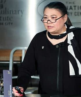 Woman wearing glasses and a black outfit speaking at a podium during an event at the Culinary Institute of America. - Olive Oil Times