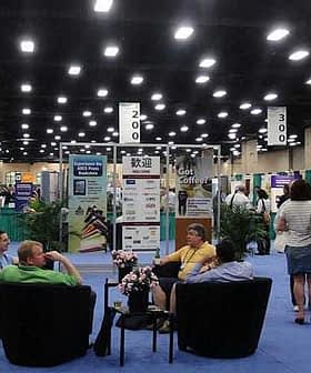Exhibition hall with attendees seated in chairs and various displays in the background. - Olive Oil Times