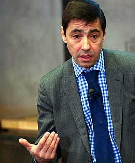 Man wearing a grey suit and blue checkered shirt speaking at an event. - Olive Oil Times