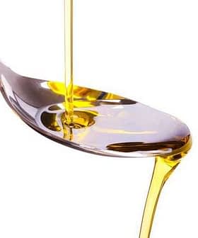 Olive oil being poured from a bottle into a stainless steel spoon. - Olive Oil Times