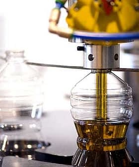 Machine filling plastic bottles with olive oil during the bottling process in a factory. - Olive Oil Times
