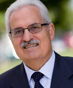 A man wearing glasses and a suit, smiling at the camera in an outdoor setting. - Olive Oil Times