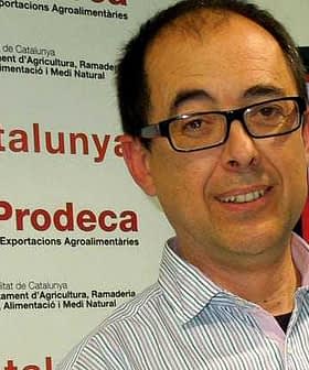 Man wearing glasses smiling at an event with Prodeca branding in the background. - Olive Oil Times