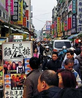 Crowd of people walking through a bustling street market in Taiwan with various stalls and signage. - Olive Oil Times