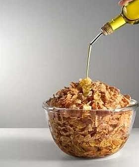 A glass bowl filled with cereal being drizzled with olive oil from a bottle. - Olive Oil Times