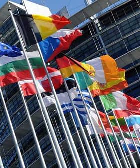 Various national flags of European countries displayed outside the European Parliament building. - Olive Oil Times