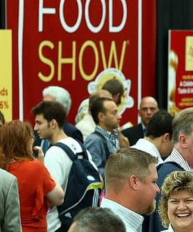 Crowd of attendees at a food show event with a large red banner in the background. - Olive Oil Times