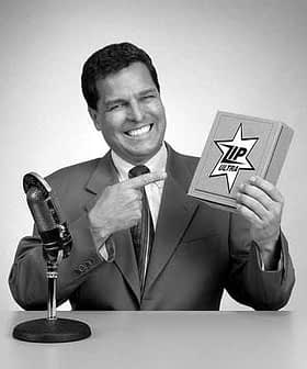 A man in a suit pointing at a product box labeled 'Tip Ultra' while standing next to a microphone. - Olive Oil Times