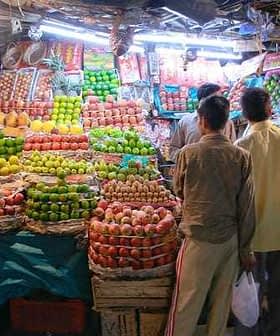 Two individuals observing a fruit stall filled with various types of apples and other fruits in baskets. - Olive Oil Times