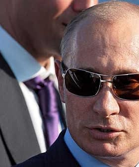 Man wearing sunglasses and a suit, with a blurred figure in the background. - Olive Oil Times