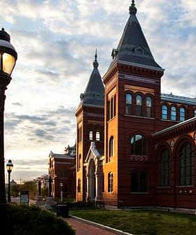 Red brick building with pointed towers and large windows under a cloudy sky. - Olive Oil Times