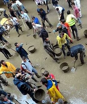 A large group of individuals using shovels and buckets in a flooded area, wearing various clothing and engaged in cleanup efforts. - Olive Oil Times