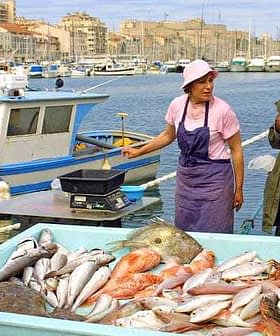 Woman and man at a fish market in Marseille with a large display of fresh fish. - Olive Oil Times