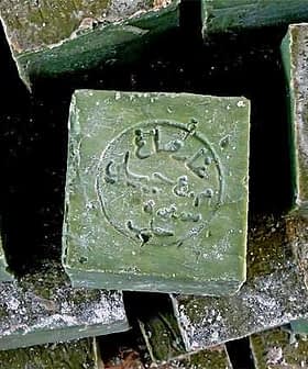 Stack of Aleppo soap bars with a stamped logo on the top bar. - Olive Oil Times