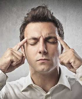 Man with closed eyes pressing fingers to his forehead, appearing to concentrate or think deeply. - Olive Oil Times