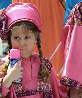 Young girl wearing a pink traditional costume holding a colorful toy in her hand. - Olive Oil Times