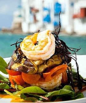 A layered dish featuring shrimp, vegetables, and greens presented on a plate. - Olive Oil Times