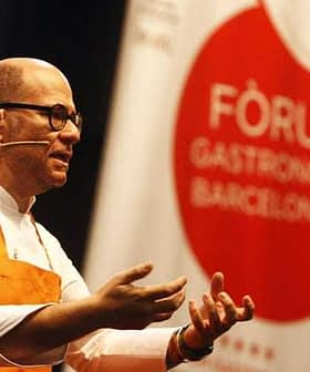 A chef gesturing while speaking at the Gastronomy Forum in Barcelona, wearing an orange apron. - Olive Oil Times