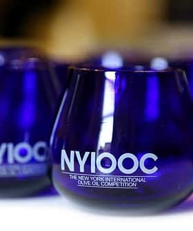 Blue glasses with the NYIOOC logo for the New York International Olive Oil Competition. - Olive Oil Times