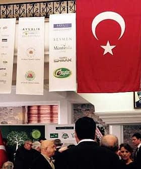 Turkish flag with a white star and crescent displayed at an indoor event with attendees. - Olive Oil Times