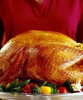 A person holding a large roasted turkey on a silver serving platter with garnishes. - Olive Oil Times
