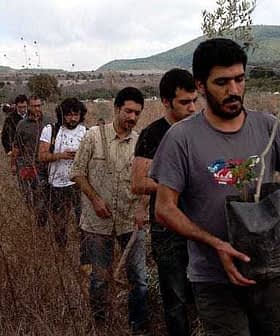 A line of individuals walking through a field, each carrying a potted plant. - Olive Oil Times