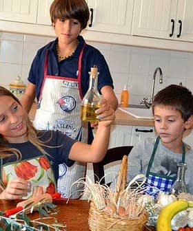 Three children in a kitchen, one holding a bottle of olive oil while others observe. - Olive Oil Times