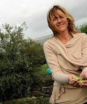 Woman with long hair wearing a beige sweater, holding olives in her hands in an outdoor setting. - Olive Oil Times