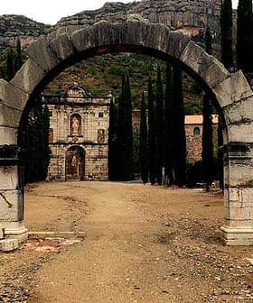 Archway with a stone structure visible in the background, surrounded by tall trees. - Olive Oil Times