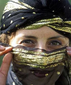 Woman with a decorative black and gold headscarf partially covering her face, revealing her eyes. - Olive Oil Times