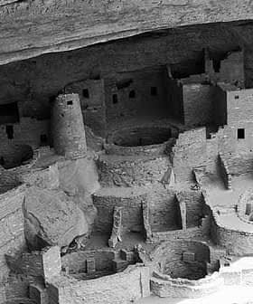Black and white image of an ancient cliff dwelling with circular and rectangular structures. - Olive Oil Times