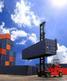 Red forklift lifting a blue shipping container at a cargo yard with stacked containers in the background. - Olive Oil Times