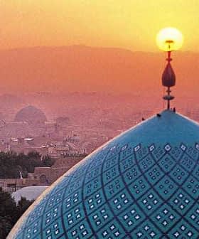 A blue dome with intricate patterns and a sun setting in the background over a city skyline. - Olive Oil Times