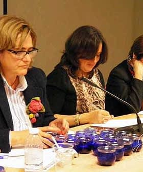 Three women seated at a conference table with blue tasting cups in front of them, engaged in discussion. - Olive Oil Times