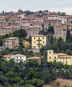 A scenic view of a Tuscan village with stone buildings and terracotta roofs surrounded by greenery. - Olive Oil Times