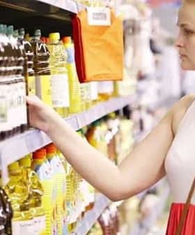 Woman examining bottles of cooking oil on a supermarket shelf. - Olive Oil Times