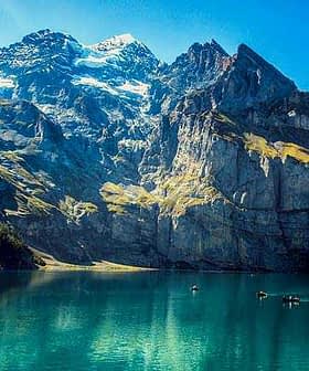 Scenic view of a mountain landscape with a clear blue lake in the foreground and rocky peaks in the background. - Olive Oil Times