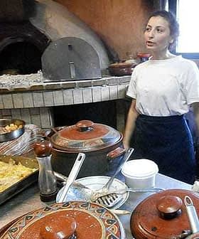 Woman standing in a kitchen with various cooking pots and an oven in the background. - Olive Oil Times